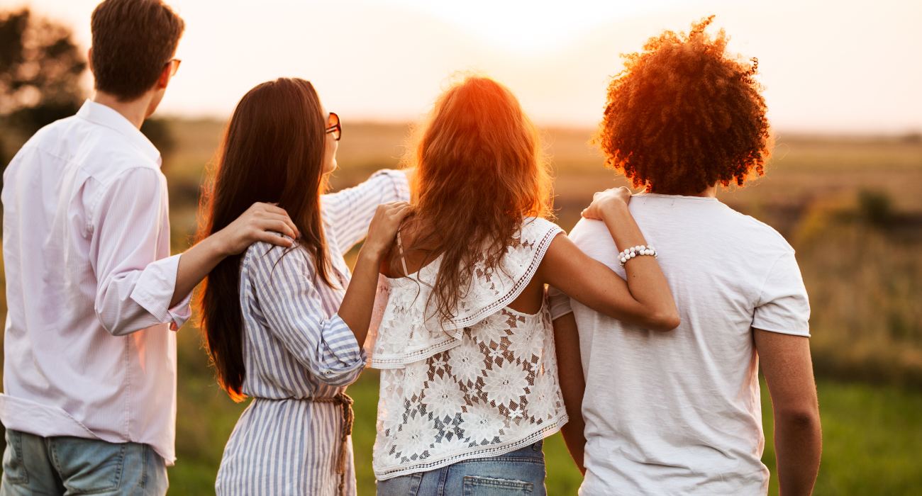 Quatre amis enlacés face au soleil couchant dans un champ